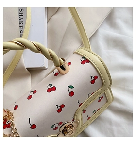 Detail of yellow cherry print bag featuring twisted handle and gold chain strap