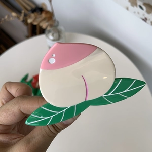 Dettaglio di un fermaglio per capelli in acetato a forma di pesca rosa con foglie verdi