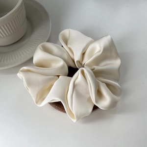 Close-up of premium satin scrunchie in cream on a wooden display stand for hair styling
