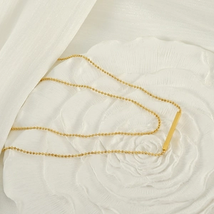 Detail of 18K gold T-bar pendant necklace on a decorative white embossed floral base