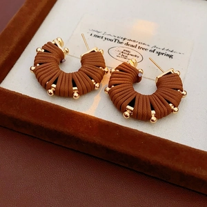 Detailed view of U-shaped brown leather earrings with gold beads in a jewelry box