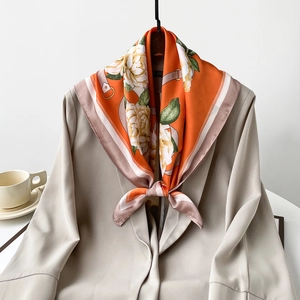 Silk-like floral scarf in orange with white flowers tied elegantly on a grey blazer