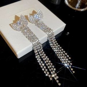 Macro detail of silver bow drop earrings with long rhinestone tassels on a jewelry box
