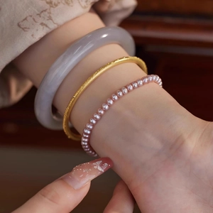 Close-up of stacked lavender pearl bracelet, gold metal bangle and violet jade stone bangle