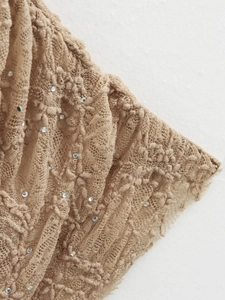 Détail macro de dentelle florale beige et strass scintillants sur robe en mesh