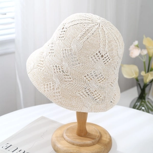 Detail of beige crochet bucket hat showing hollow knit diamond texture on wooden stand