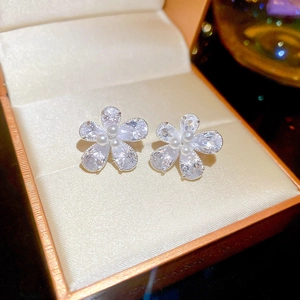 Close-up of flower-shaped stud earrings with zircon and pearl in an orange jewelry box