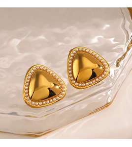 Détail de boucles d'oreilles triangles dorées avec perles sur plateau verre