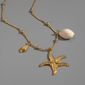 Detail of gold bead chain necklace with starfish, gold shell, and white cowrie pendants