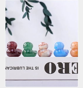 Group of five natural crystal duck carvings in various gemstones displayed on a book