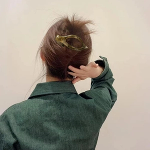 Detail of dark green oval shark clip holding hair in a sleek back-up hairstyle