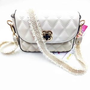 Detail of white quilted crossbody bag with golden clover clasp and tassel strap