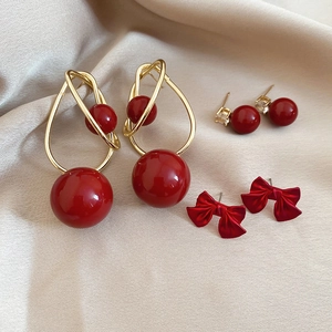 Detail of red bead earrings and bow studs on a champagne silk fabric backdrop