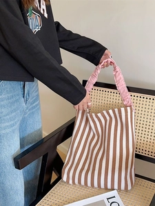 Canvas tote bag with brown and white stripes and pink ruffled straps on a rattan chair