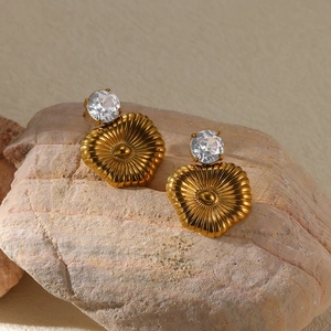 Detailed view of gold plated heart earrings with zircons on a textured stone base