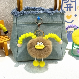 Cute fuzzy brown plush keychain with yellow legs hanging on a blue denim tote bag