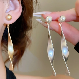 Détail de boucles d'oreilles pendantes en métal mat torsadé en or et argent design