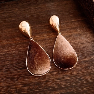 Close-up of teardrop earrings featuring brown velvet inlay and 18k gold plated edges