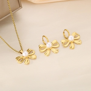 Detail of golden bow pendant necklace and earrings set with white pearls on silk fabric