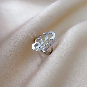 Detailed close-up of a silver floral cutout ring on elegant beige pleated silk fabric