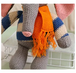 Détail d'un doudou éléphant en maille avec un pull rayé et une écharpe à pompons orange