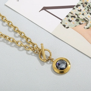 Macro shot of gold OT buckle necklace with dark crystal pendant on grey textured surface