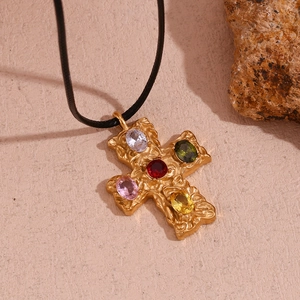 Macro detail of gold-plated cross pendant with colorful zircons and hammered texture