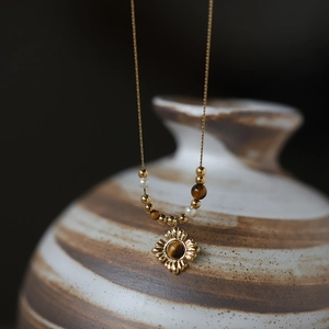 Gold vintage necklace with tiger eye beads and sunburst pendant on ceramic vase