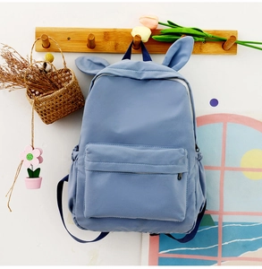 Blue rabbit-eared backpack hanging on a wooden hanger with a decorative floral backdrop