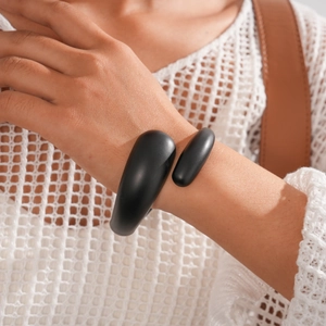 Detail of a matte black acrylic irregular geometric open cuff bracelet on a female wrist