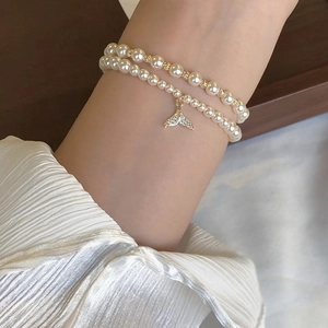 Macro detail of double-layer pearl bracelet featuring a sparkling gold fishtail pendant