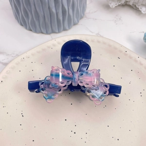 Detail of a navy blue acetate claw clip with a pink-blue lace bow on a ceramic plate