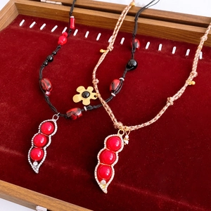 Detail view of red pea pod pendants with crystals on black and khaki braided cords