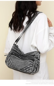 Detail of washed denim crossbody bag featuring multiple zipper pockets and adjustable strap