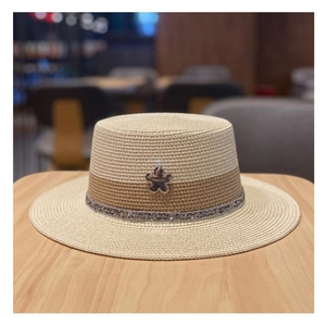Dettaglio cappello di paglia a testa piatta con fascia di paillettes e ciondolo a fiore