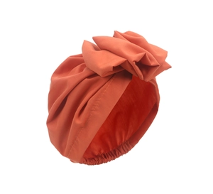 Detail of orange-red turban hat featuring a pleated fabric flower and elastic band