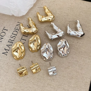 Flat lay of abstract metallic stud earrings in gold and silver on textured fabric