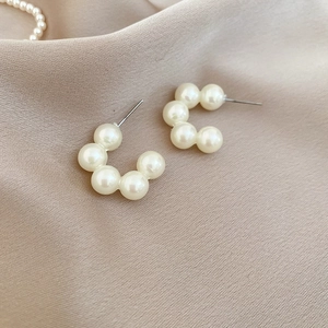 Detail view of C-shaped drop earrings with polished white pearls on elegant satin