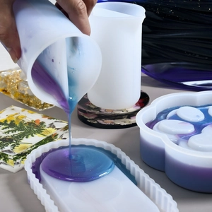 Macro view of dual-layer silicone measuring cup pouring blue resin into wavy oval DIY mold