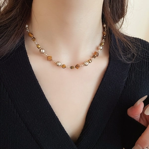 Nahaufnahme der Perlenkette aus Tigerauge und Gold am Hals betont den Schlüsselbeinbereich