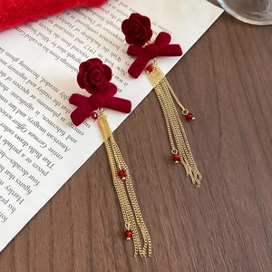 Detailed view of velvet red rose earrings with golden tassel chains and bead accents