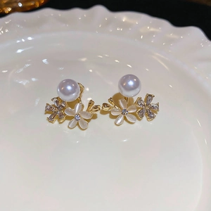 Close-up of floral pearl earrings with opal petals and rhinestones on a ceramic dish