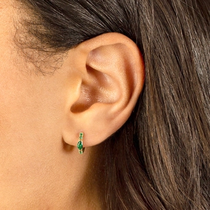 Close-up of gold hoop earrings with emerald-cut green zircons on a model's ear
