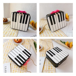 Detail view of piano keyboard bag with pink bow and gold chain strap on plaid background