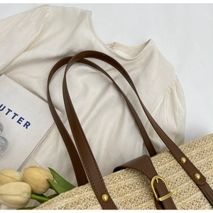 Straw beach tote with brown leather straps and metal rivets on a minimalist background