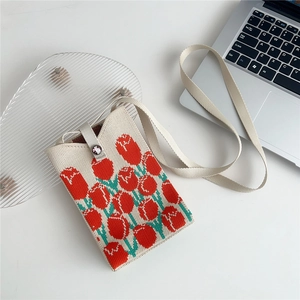 Close-up of cream knitted phone bag with red tulips on white desk with laptop