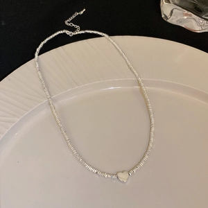 Detailed view of silver beaded necklace with heart pendant on a white ceramic plate