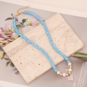 Close-up of blue clay beads necklace with heart pendant and faux pearls on stone background