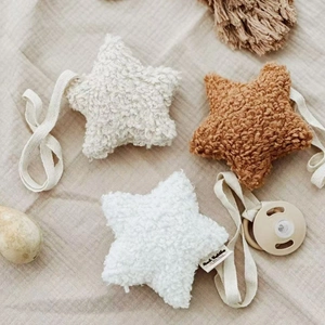 Detail of plush star-shaped pacifier clips with Mushie labels on linen background
