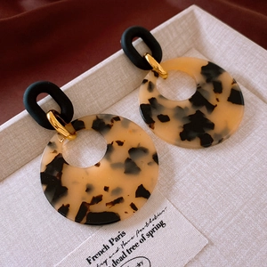 Close-up of leopard print acrylic earrings with gold metal and matte black details